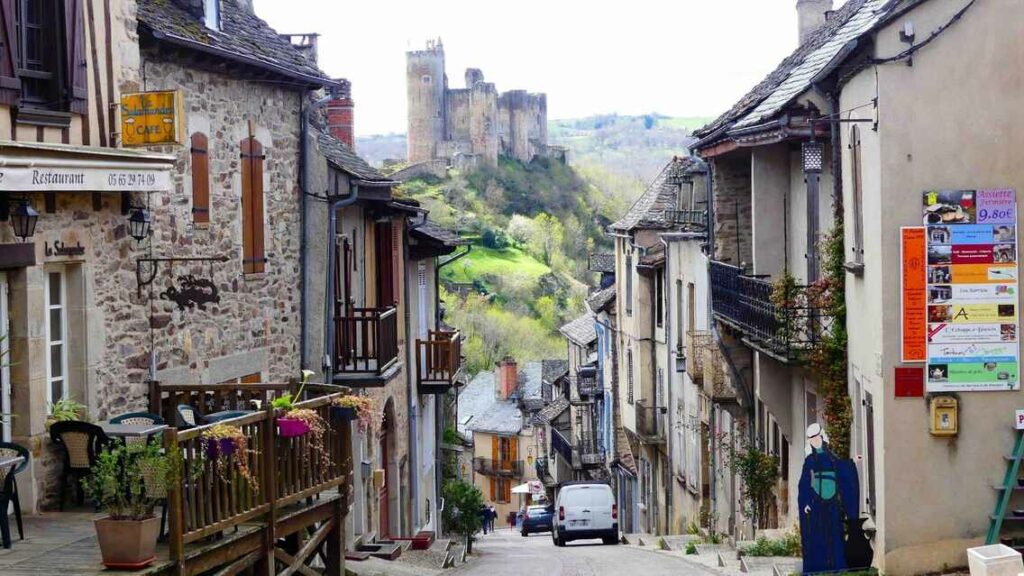 Ruelle pavée de Najac (Aveyron) bordée de maisons en pierre et terrasse, avec le château médiéval dominant la vallée.