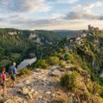 Deux randonneurs sur un sentier dominant Najac et son château médiéval perchés au-dessus de l'Aveyron.
