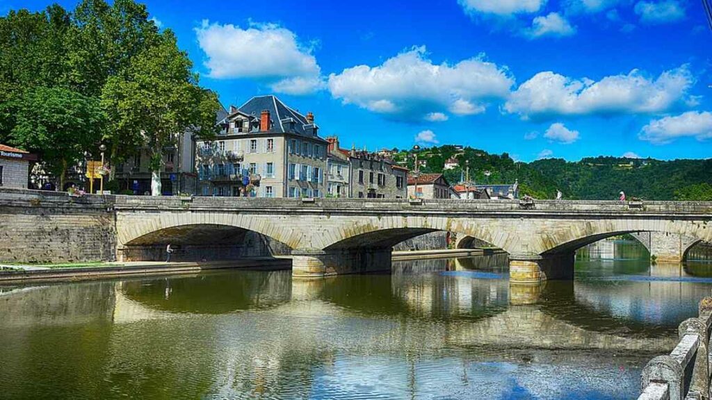 Pont en pierre à arches sur la rivière, façades anciennes et arbres sous un ciel bleu à villefranche de Rouergue (Aveyron)